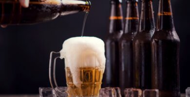 Cerveja artesanal: quais as diferenças da comum e seus benefícios 4 garrafas de vidro de cerveja com vidro e gelo no fundo escuro